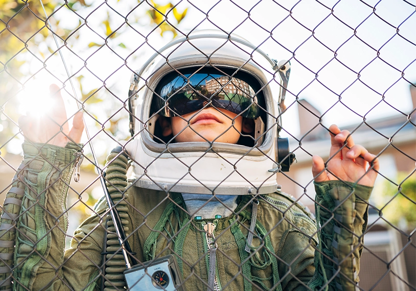 a kid dressed as an astronaut looks through a fence