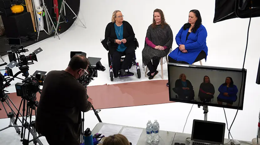 Three females and a cinematographer get ready to film in a studio.